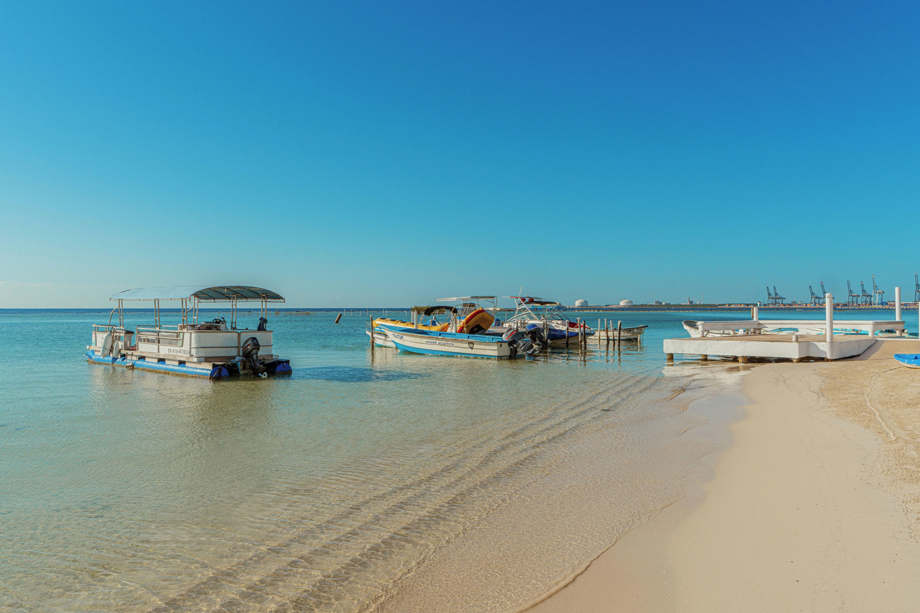 A beach with boats docked, a clear sky, and calm water.