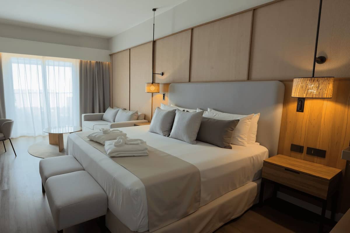 Quarto de hotel moderno com uma cama grande, uma escrivaninha, uma cadeira e um sofá.