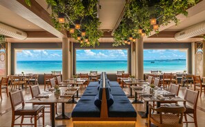 Un restaurante con vista al océano, mesas con sillas y plantas colgantes.