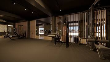A modern gym with various exercise equipment, a large mirror, and a view of the cityscape through a large window.