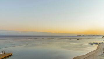A beach with a wooden pier and boats, a sandy shore, and a calm sea.