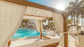 A poolside area with a covered seating area, a pool, and palm trees in the background.
