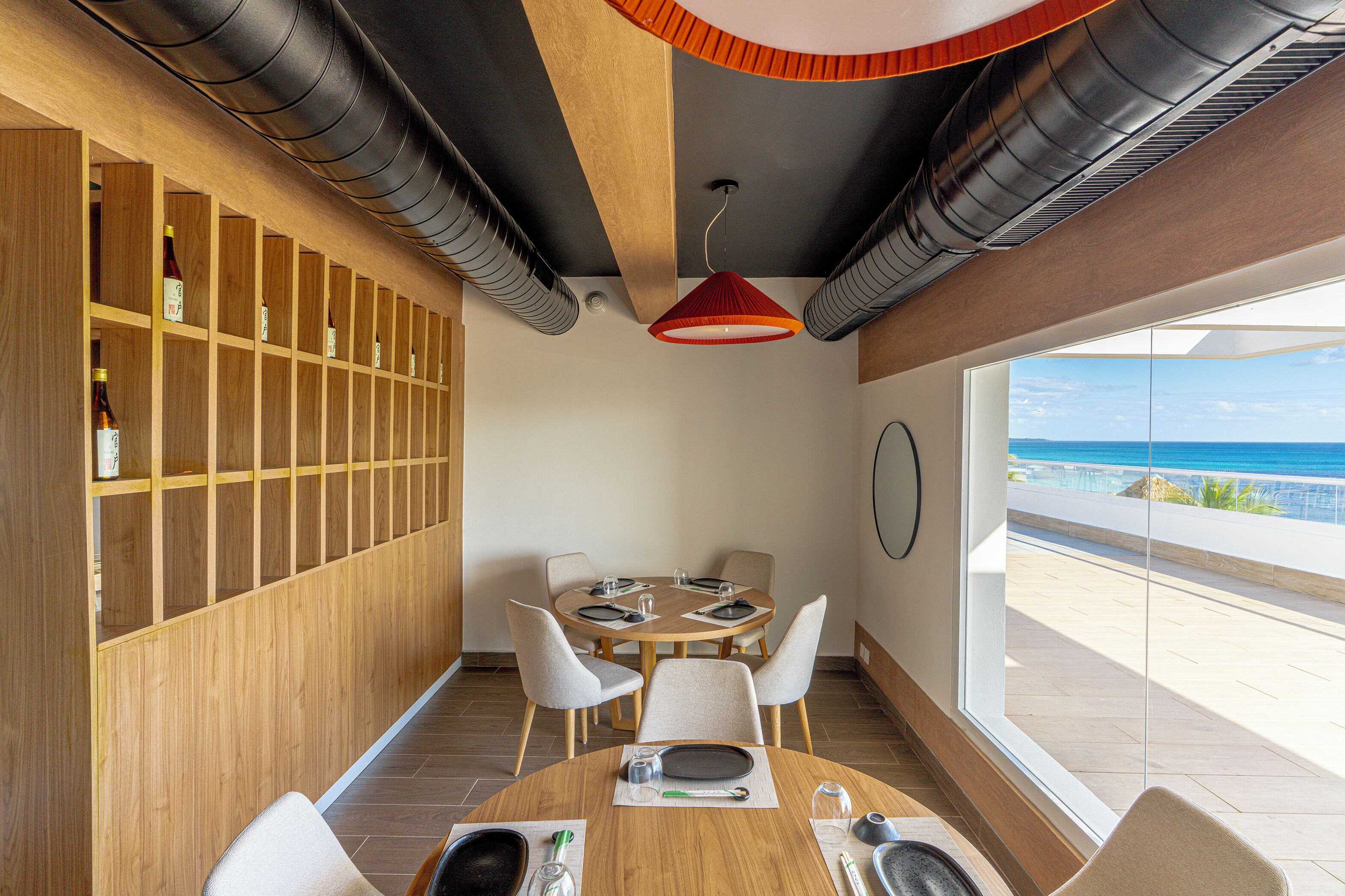 Un coin repas avec un mur en bois, une table ronde et des chaises. Une fenêtre offre une vue sur l’océan.