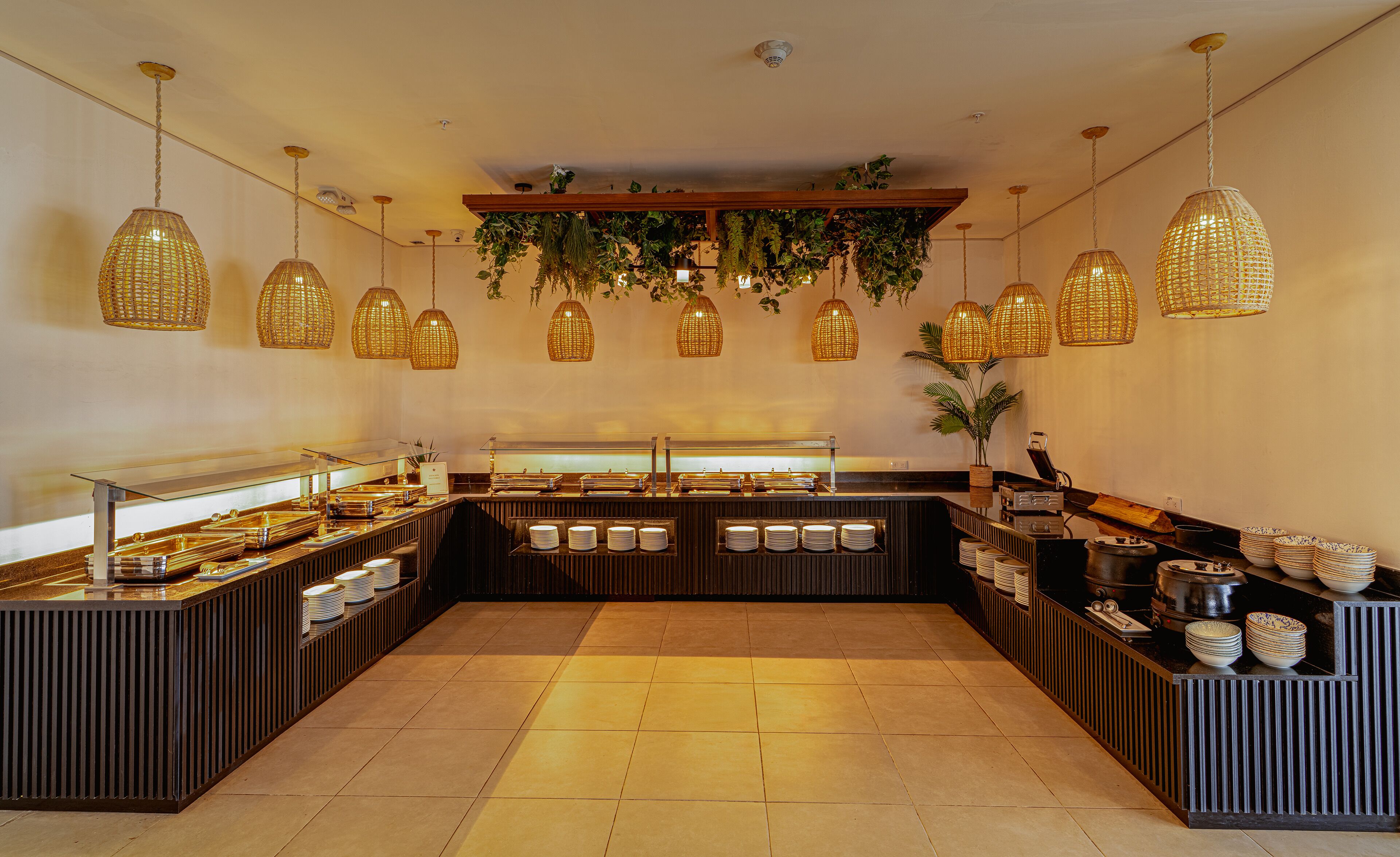 Un área de buffet con plantas colgantes, una estación central de servicio y piso de baldosas.