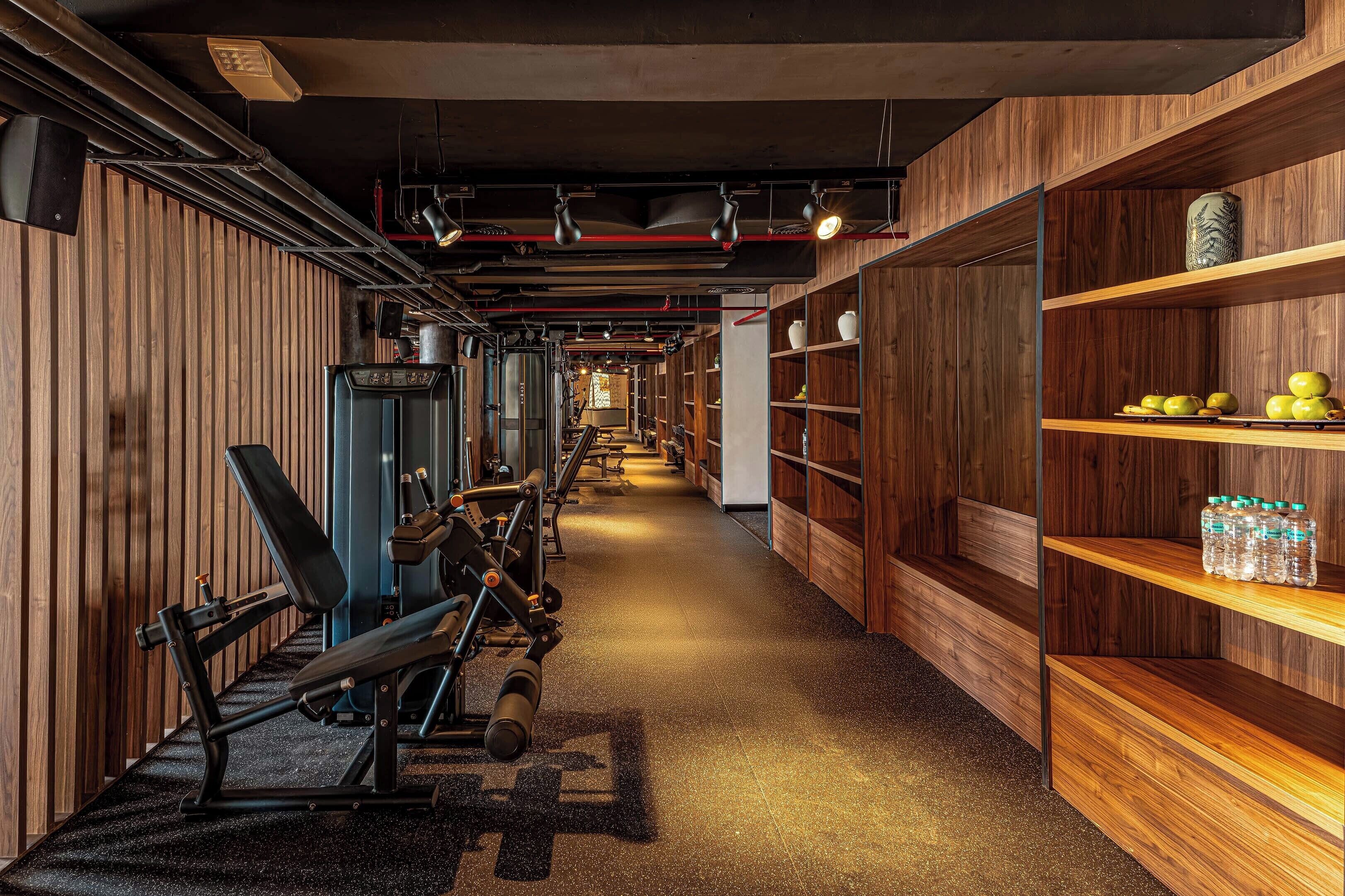 A gym with exercise equipment, wooden walls, and shelves with water bottles.