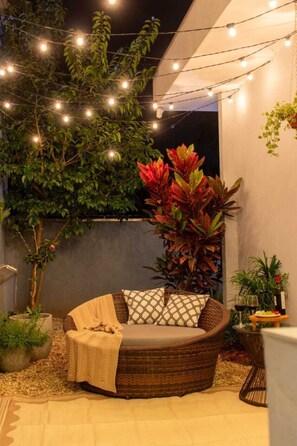 Un espace extérieur accueillant avec un canapé en osier, des coussins à motifs et des guirlandes lumineuses.