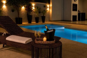 Un espace de détente aménagé au bord de la piscine, avec un fauteuil inclinable, une petite table sur laquelle se trouvent une bouteille de champagne, des verres et une bougie.