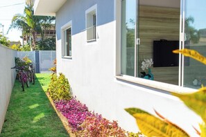 A modern house with a white exterior, a small garden with colorful flowers, and a bicycle parked outside. - GREY HOUSE | Heated Pool 240 meters from the beach (Bombinhas)