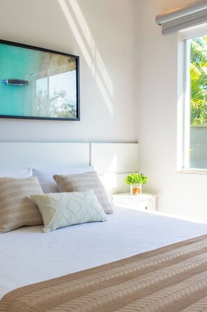 Une chambre à coucher avec un lit, des oreillers, une table de chevet, une petite plante et une fenêtre donnant sur un paysage verdoyant.