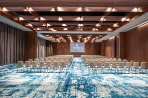 A conference room with rows of chairs, a large screen, and a wooden ceiling with lighting fixtures. - Renaissance Porto Lapa Hotel (Cedofeita)