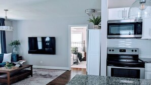 Eine moderne Küche mit Einbauofen und Mikrowelle, eine Essecke mit Holztisch und Stühlen sowie ein Wohnzimmer mit Fernseher und Sofa.