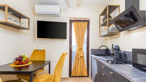 Eine kleine Küche mit Essbereich, einem an der Wand montierten Fernseher und einem Fenster mit Vorhängen.