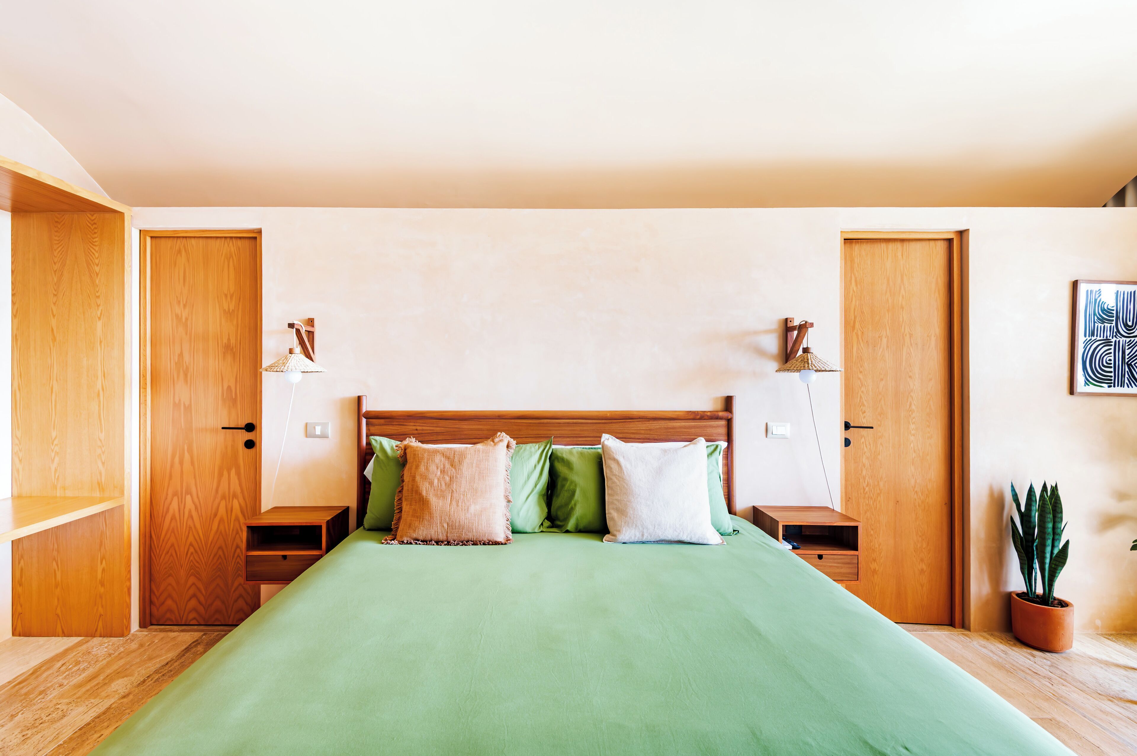 Un dormitorio con cama de madera, ropa de cama verde, dos mesitas de noche con lámparas y una planta en maceta.