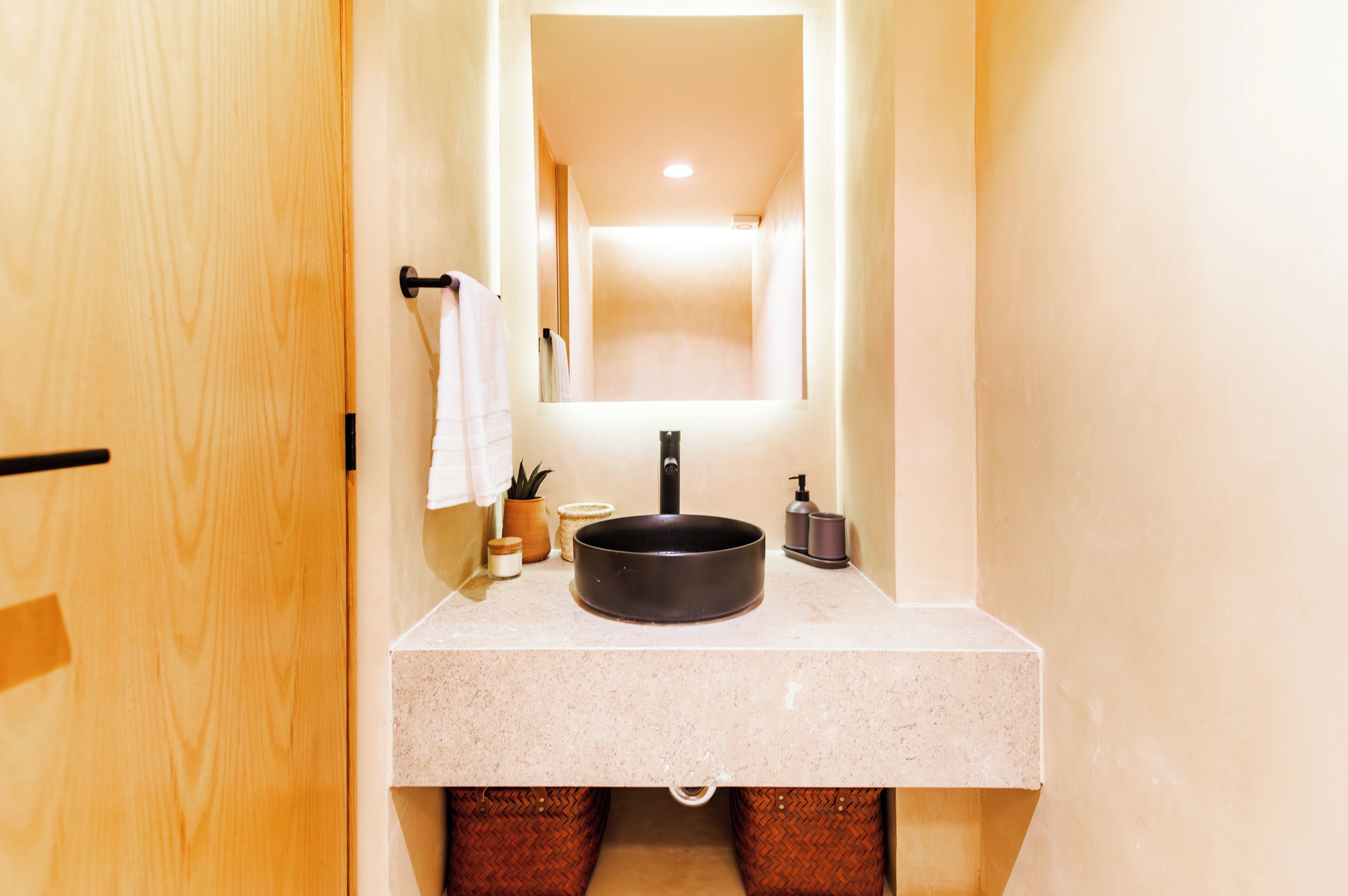 Un baño con puerta de madera, un lavabo con espejo y una toalla colgada en la pared.