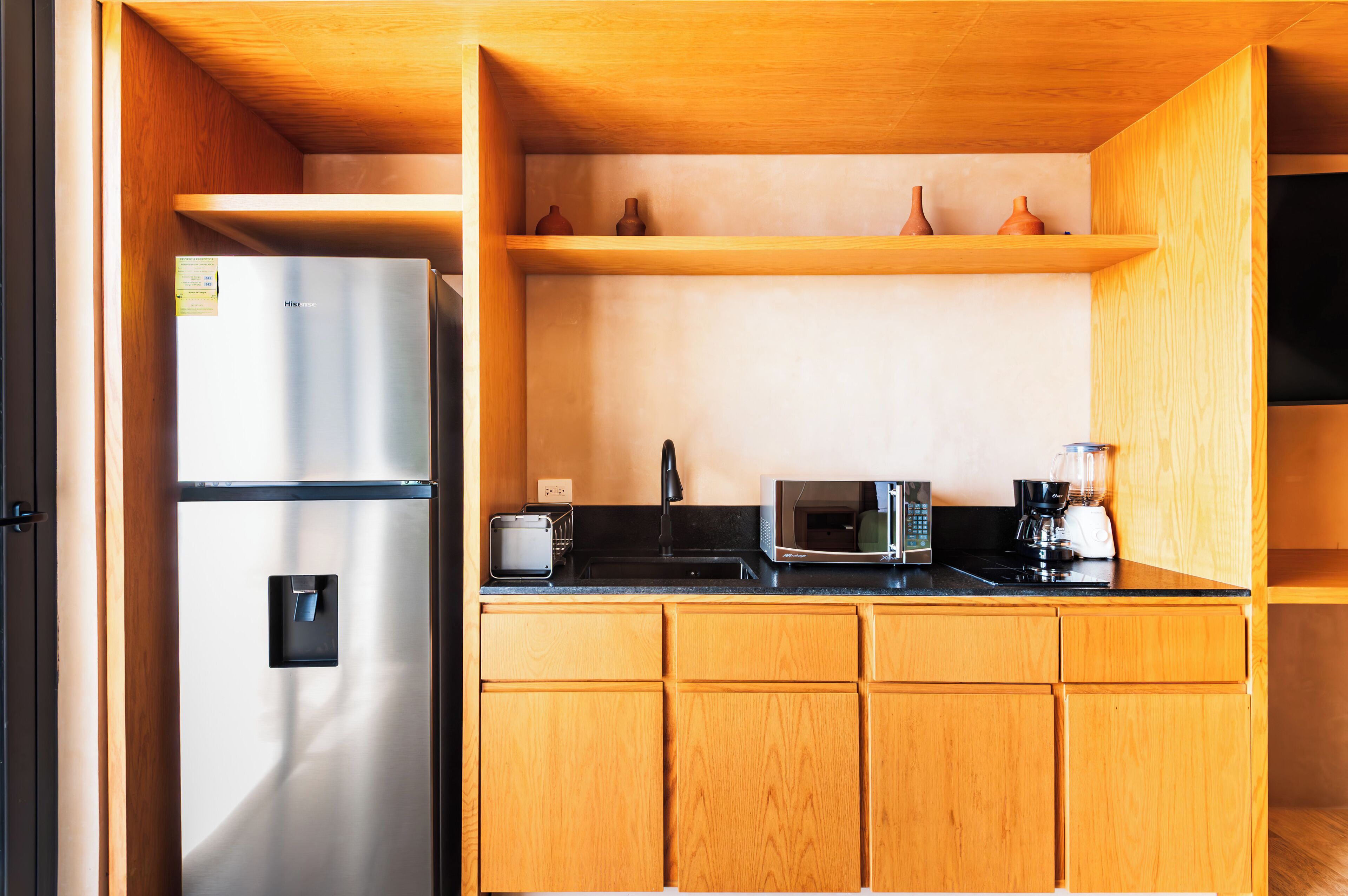 A compact kitchen with a stainless steel refrigerator, a microwave, a coffee maker, and wooden cabinets.