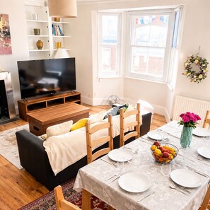A living room with a TV, sofa, dining table set, and a window with a view.
