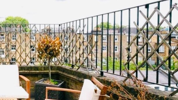 A balcony with a wooden table and two white chairs, a potted plant, and a view of buildings in the background. - The Chelsea Ambassadorial Executive Penthouse (London)