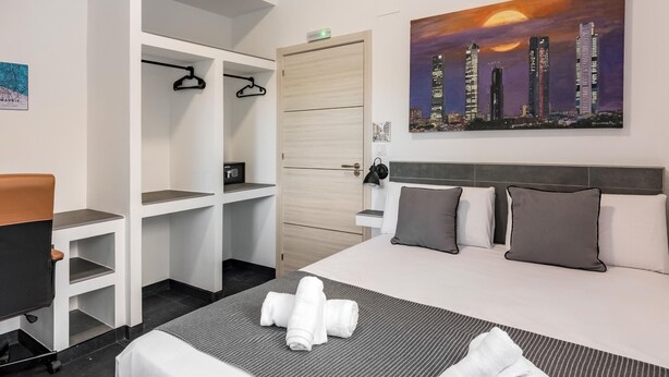 A hotel room with a bed, a desk, a wardrobe, and a cityscape painting. - Charming Madrid Las Rosas, 2 habitaciones (Madrid)