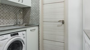 A compact laundry room with a washing machine, a sink, and a door with a handle. - Charming Madrid Las Rosas, 2 habitaciones (Madrid)
