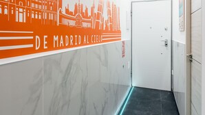 A corridor with a cityscape mural, a white door, and a green exit sign. - Charming Madrid Las Rosas, 2 habitaciones (Madrid)