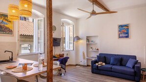 Una sala de estar con un sofá azul, vigas de madera, un ventilador de techo y vistas al exterior a través de una ventana.
