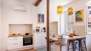 Una cocina moderna con horno empotrado, microondas y cafetera. Hay taburetes y una zona de bar con una botella de agua y un vaso.