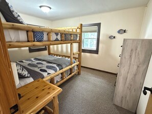Een slaapkamer met een stapelbed, een houten bureau, een kledingkast en een raam met zonwering.