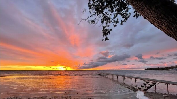 Een zonsondergang boven een wateroppervlak met een houten steiger die het water in reikt.