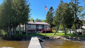 Een houten steiger die leidt naar een huis met een rood terras en een Amerikaanse vlag.