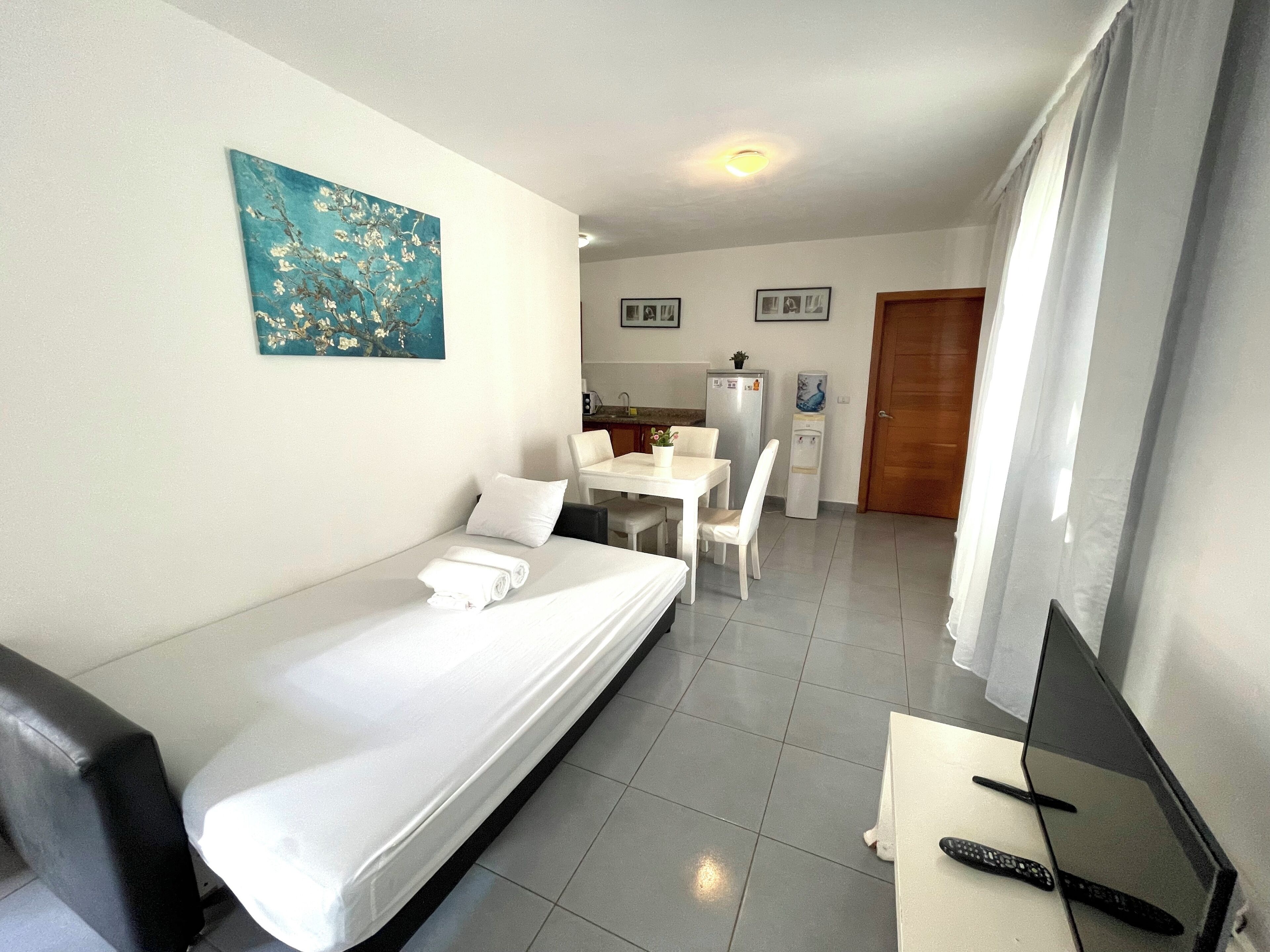 A hotel room with a bed, a desk, a chair, a TV, and a refrigerator.