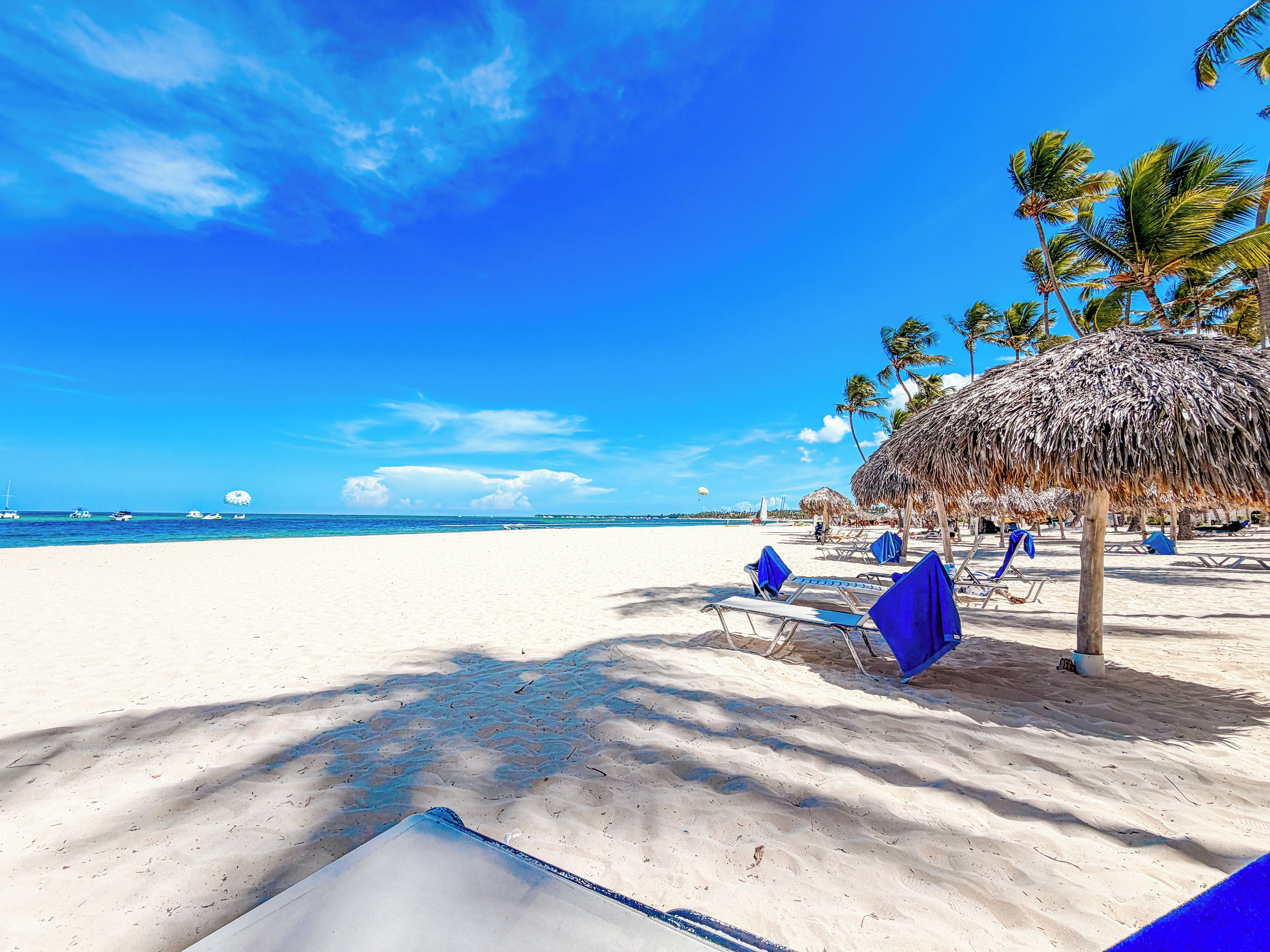 Ein Strand mit weißem Sand, blauem Himmel und Palmen.