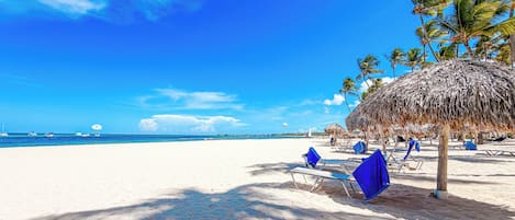 A beach with white sand, clear blue sky, and palm trees.
