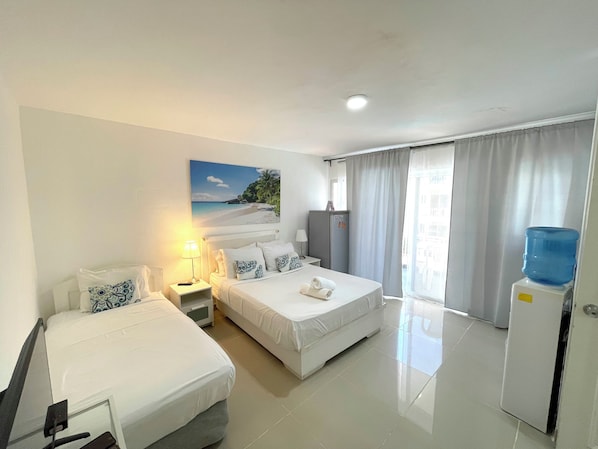 Een hotelkamer met twee bedden, een bureau, een lamp, een waterdispenser en een schilderij van een strandgezicht.
