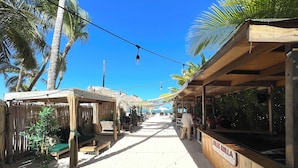 A beachside walkway with thatched-roof structures, palm trees, and a wooden bar area. - CARIBBEAN STUDIOS POOL BEACH & SPA  (Punta Cana)