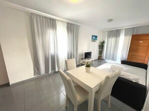 Een hotelkamer met een bed, een televisie, een klein tafeltje met stoelen, een plant in pot en een raam met gordijnen.