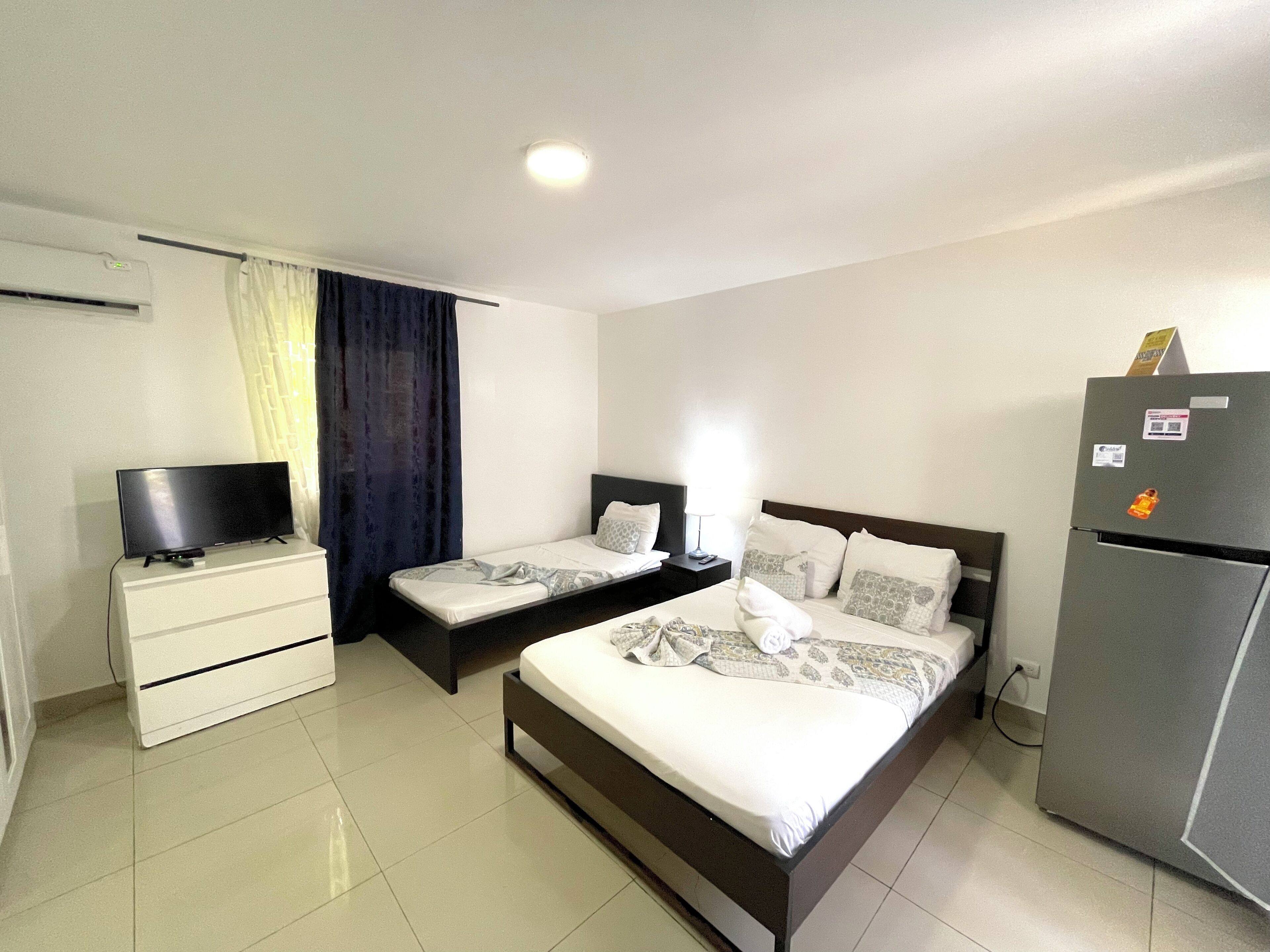 A hotel room with two single beds, a television, a refrigerator, and a small desk with drawers.