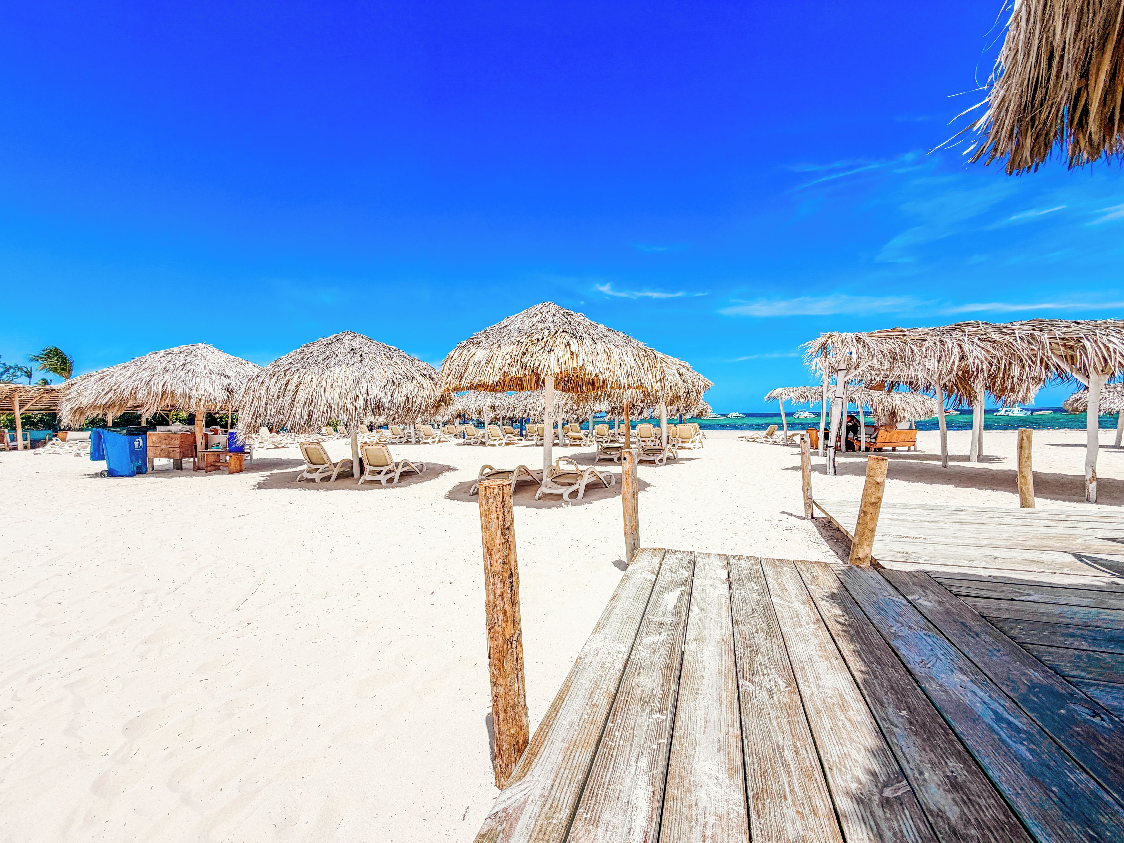 A beach with thatched umbrellas and lounge chairs.