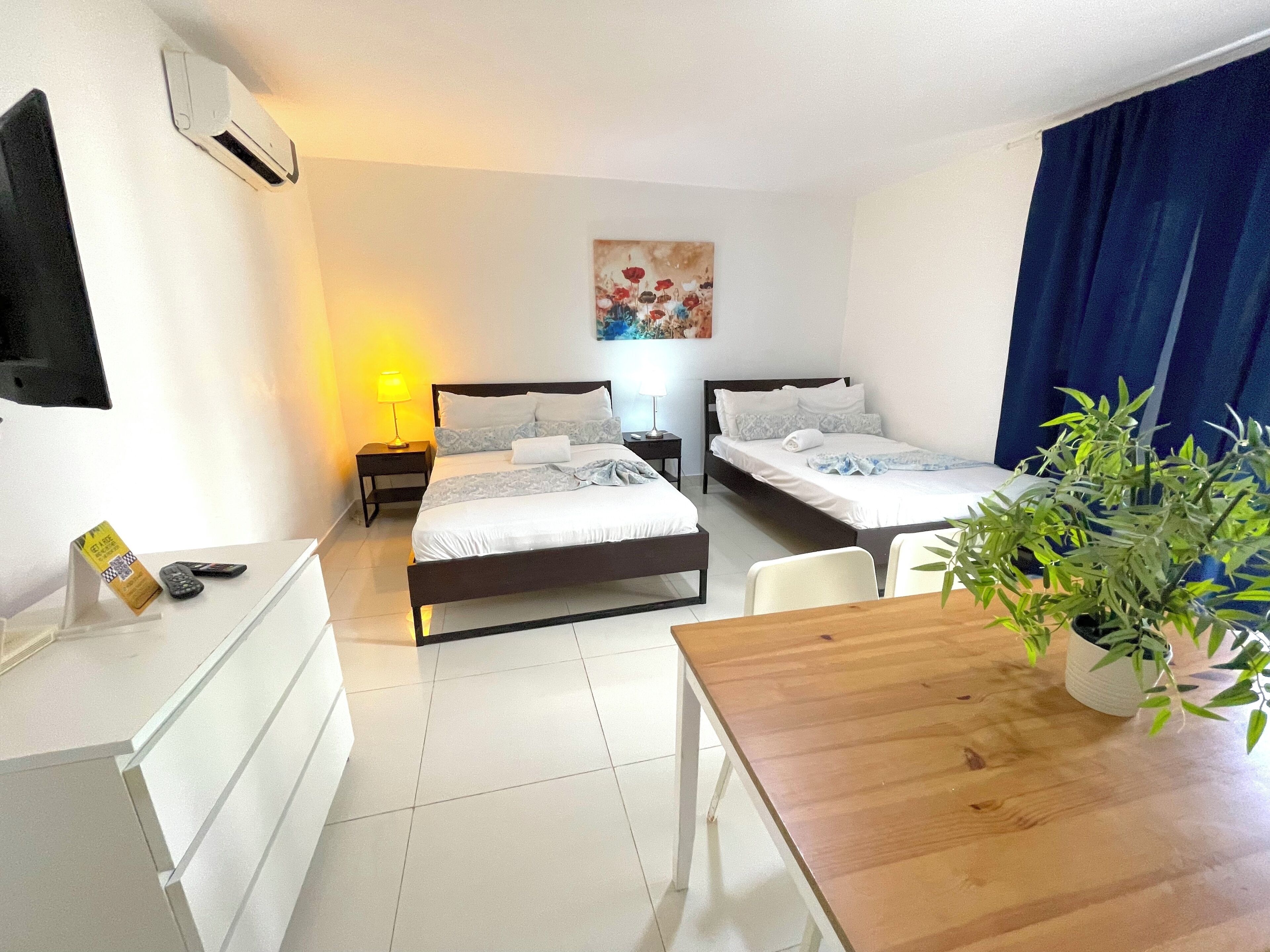 Een hotelkamer met twee bedden, een bureau, een stoel, een lamp, een kamerplant en een schilderij aan de muur.