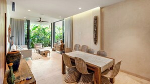Un comedor espacioso con una larga mesa de madera y sillas de mimbre, un sofá y una mesa baja al fondo.