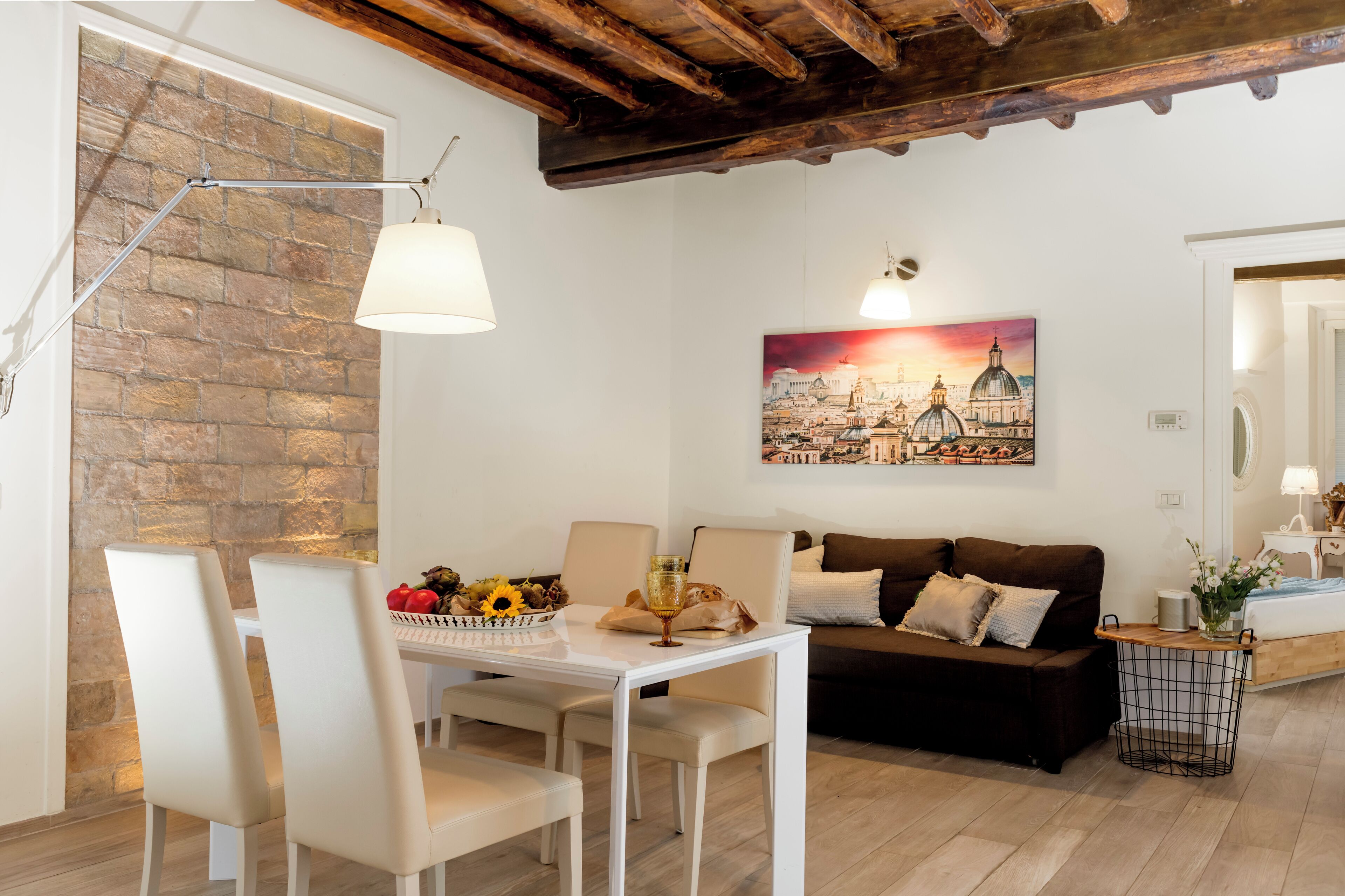 Un comedor con una mesa y sillas blancas, un sofá marrón y un cuadro de un paisaje urbano.