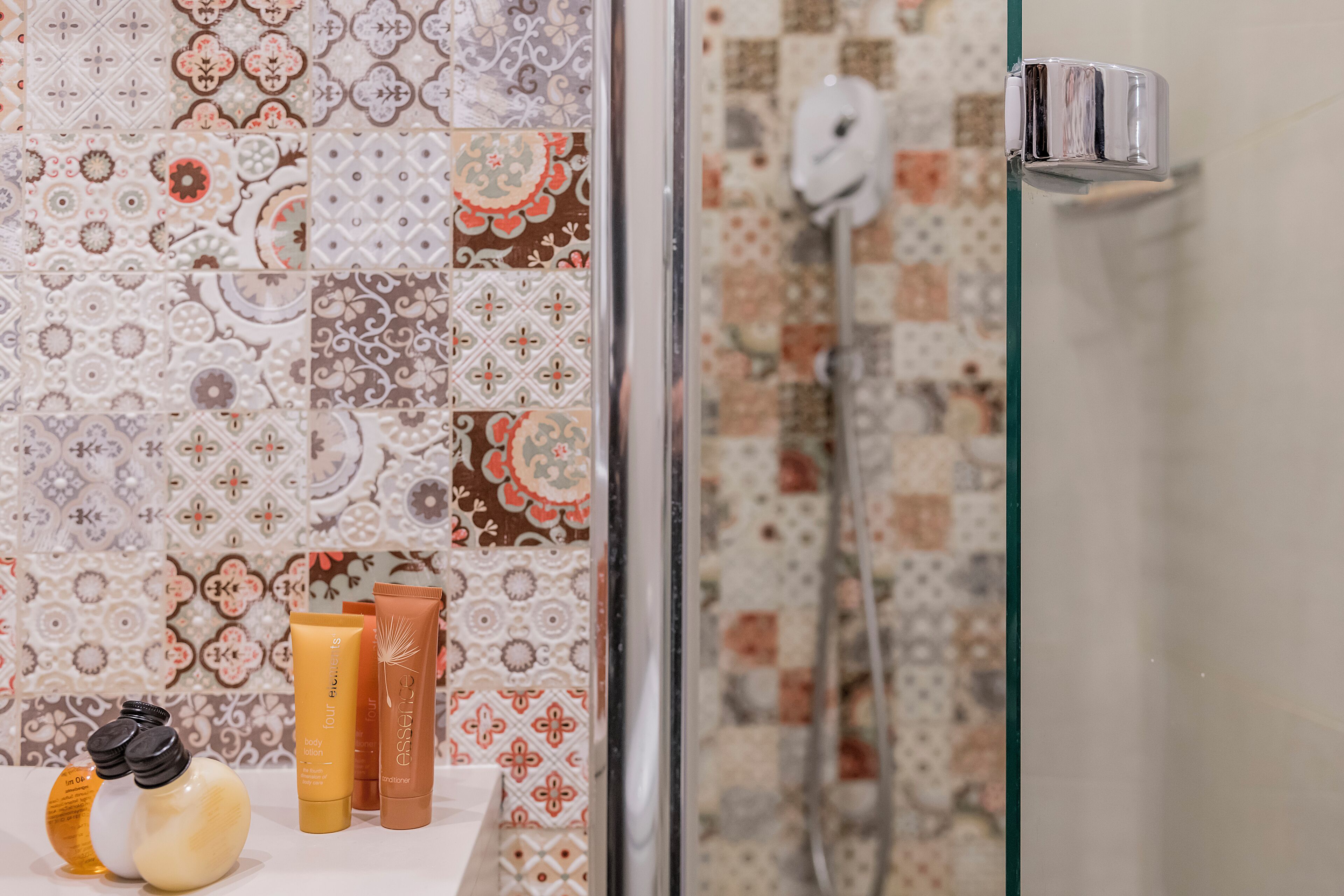 A bathroom with patterned tiles, a glass shower door, and various toiletries on the counter.