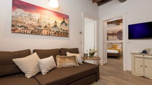 A living room with a brown sofa, a painting of a cityscape, a TV, and a wooden floor.