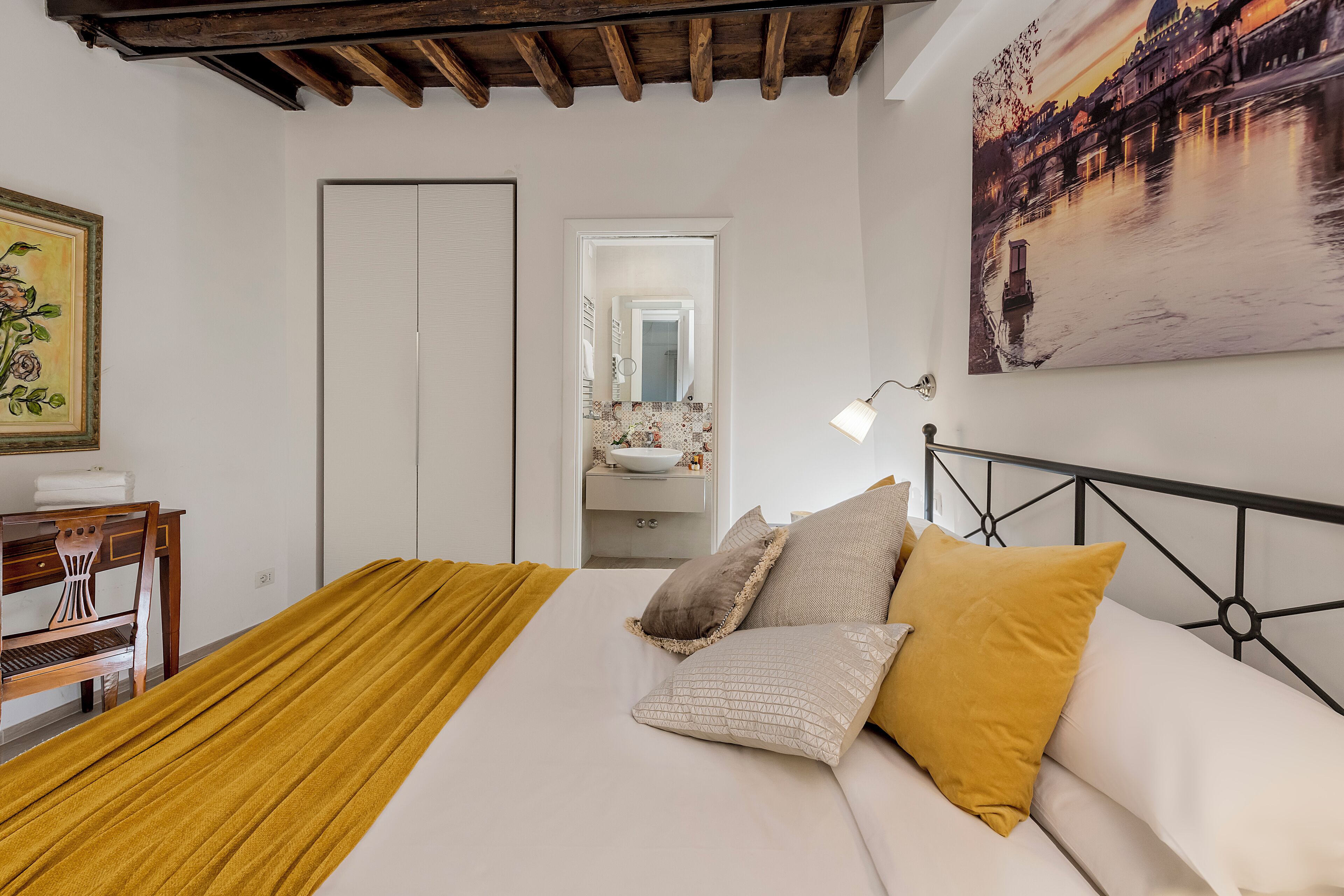 A bedroom with a bed, a desk, a chair, a mirror, and a painting on the wall.