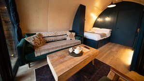 A cozy room with a sofa, a small table with a teapot, and a bed with neatly made pillows.