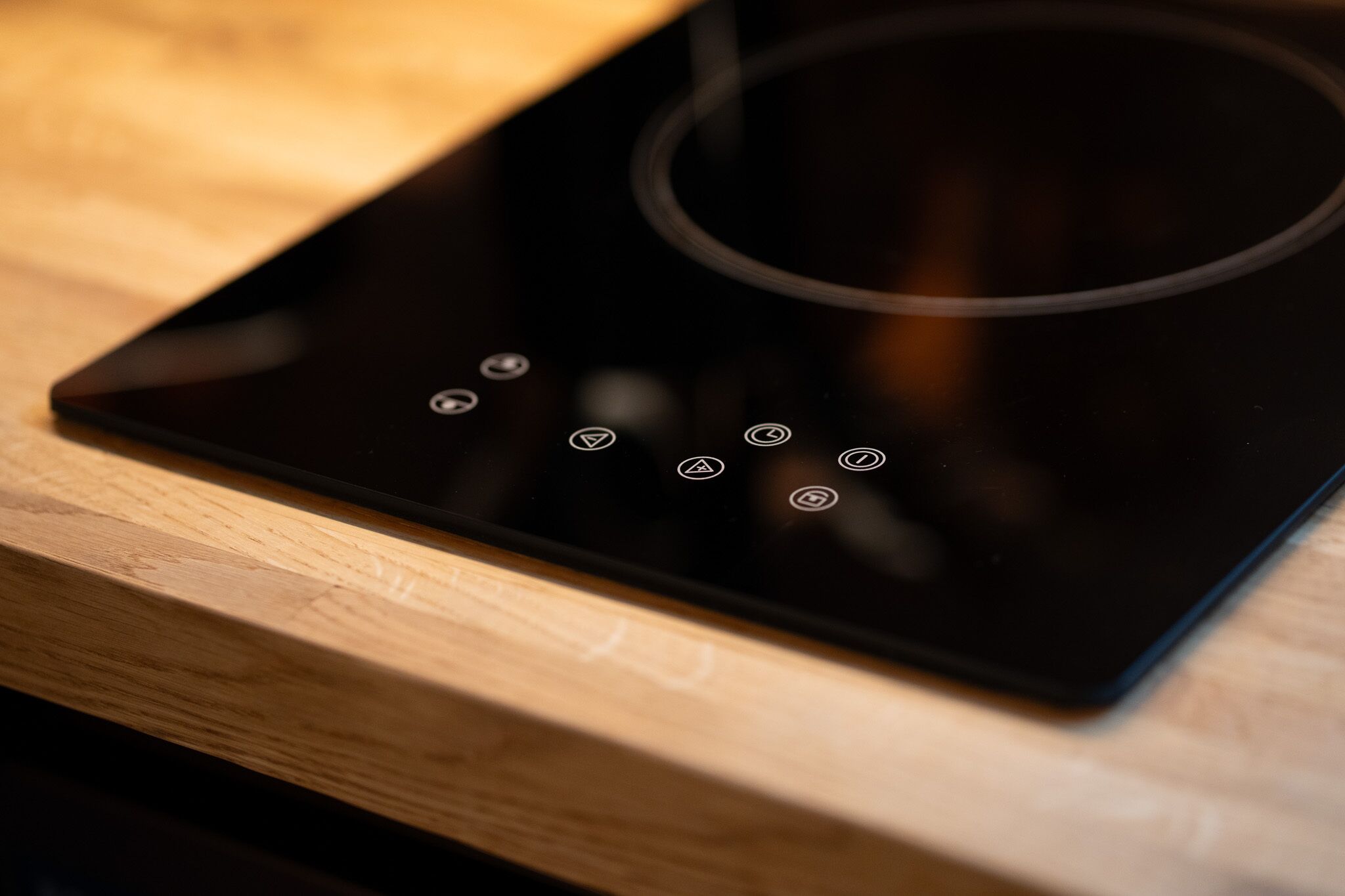 A black induction cooktop with control buttons on a wooden surface.