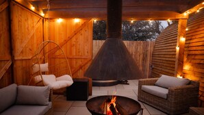 An outdoor patio with wicker furniture, a fire pit, and string lights.