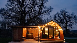 A cozy, wooden cabin with a large, curved glass door, a small porch area, and a chimney.