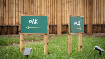 Two directional signs labeled "OAK" and "HOLLY" on a grassy area with a wooden fence in the background.