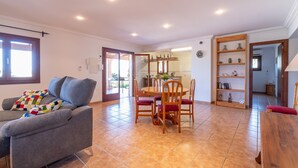 Una sala de estar con sofá, una mesa de comedor con sillas y una cocina visible a través de una puerta abierta.