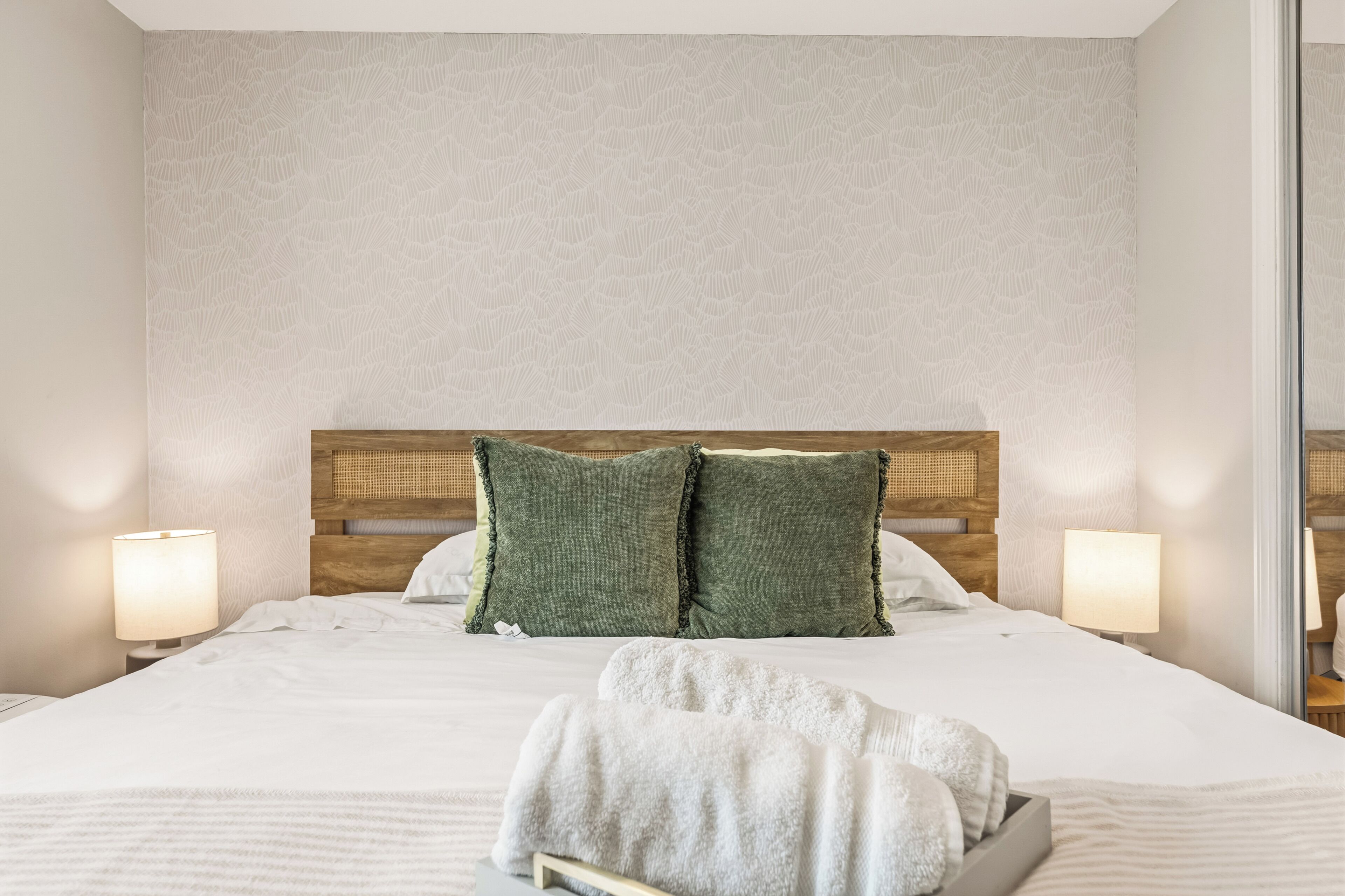 Una cama bien hecha con almohadones verdes, un cabecero de madera y dos lámparas de noche.
